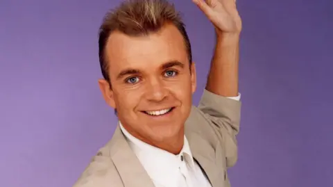 Wayne Dobson in his 1990s heyday wearing suit jacket and spiky hair