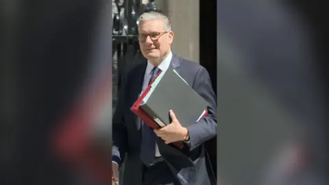 UK PM Keir Starmer wearing suit and holding binders