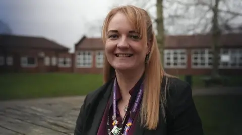 Ann Gannon / BBC Samantha, who has long blond hair, smiles at the camera wearing a burgundy shirt and black jacket. 