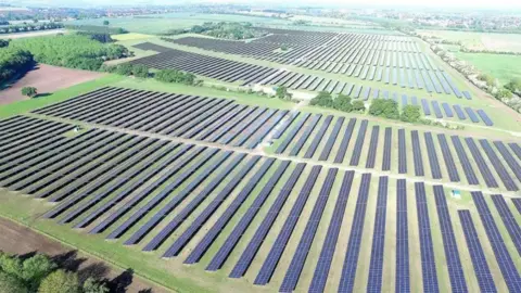 Artist impression of the site showing an aerial view of rows of solar panels in green fields surrounded by trees