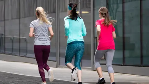 Three women running, one with blonde hair, a grey top and maroon leggings, one with dark hair, a turquoise top and teal leggings and the third with brown hair, a pink top and grey leggings