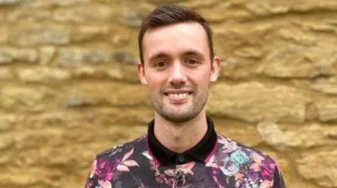 Leon McAnally Leon McAnally with short dark hair wearing a flowery shirt