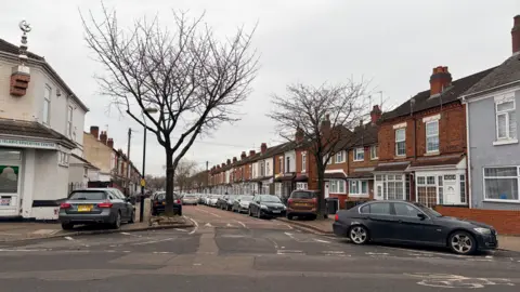 Cars parked on the side of the road and on the pavement on a residential street.