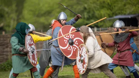 Re-enactors wearing Viking Helmets and holding spears and shields in mock battle