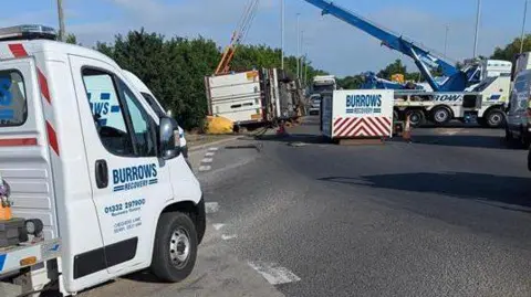 National Highways Recovery teams craning the overturned lorry from the side of a roundabout