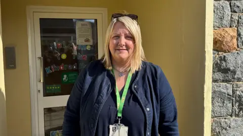 Blonde woman standing in front of a door in a blue dress and denim jacket