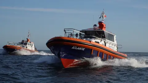 A 16.6 metre pilot boat called Atlantic with a dark blue hull, orange trim and white cabin speeds across the sea with a similar boat called Arrow in the background.