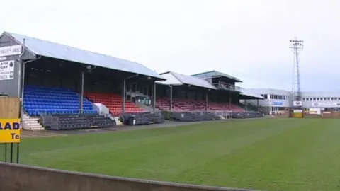 BBC A rugby pitch with red and blue spectator stands along the left hand side