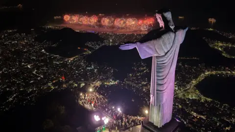 Getty Images Vista aérea do Cristo Redentor enquanto fogos de artifício para celebrar o Ano Novo explodem na praia de Copacabana durante as celebrações no Rio de Janeiro, Brasil