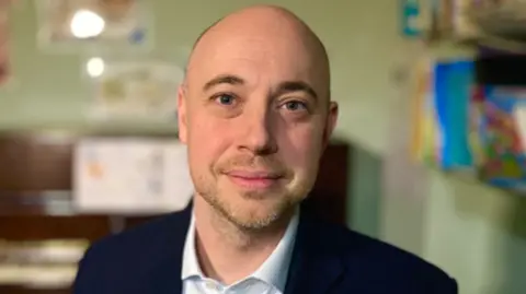 Martin Giles/BBC Head and shoulders image of Adam Taylor wearing a blue suit jacket and white shirt