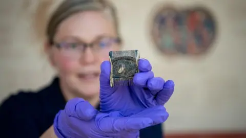 A woman wearing blue gloves holds up an old comb which has thin teeth at one end and bigger ones at the other