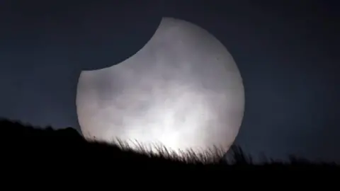 PA Media A picture of a partial eclipse. It is large and pictured behind grassland.