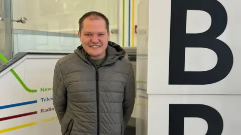 Jake Banbury smiling at the camera and wearing a grey coat.