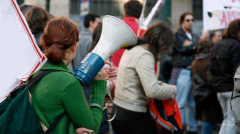 Woman with a speaker in a green top at a protest outside a university
