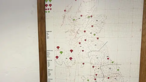 A map of the UK on a wall with red and green pins attached to various areas of it