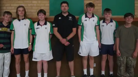 Six schoolboys, in sports clothing, stood either side of a teacher - who is also in sportswear.