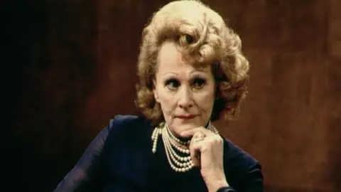 Fanny Cradock with her hand to her chin. She is wearing a pearl necklace