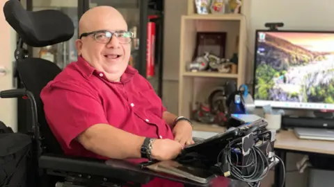 Mark Norman Peter Zein in his wheelchair with the technology the uses to be able to speak.