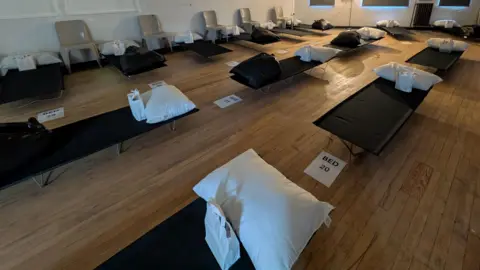 Emmanuel House Camp beds with pillows are lined up in rows