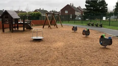 Strathfoyle play park has a number of slides and swings, as well as climbing frames. A number of benches are scattered across the site that is fenced off.