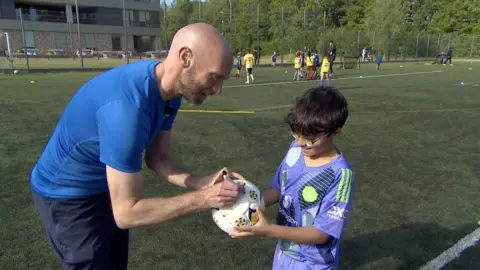 Steve Hubbard/BBC Luke Chadwick, in blue T-shirt, signs a football for a child wearing a mauve Manchester United shirt.
