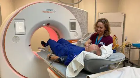 Man and nurse lying down to enter BBC CT scanner