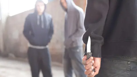 Getty Images A stock photo of two men being confronted by man with knife. All people in the photo are anonymous.