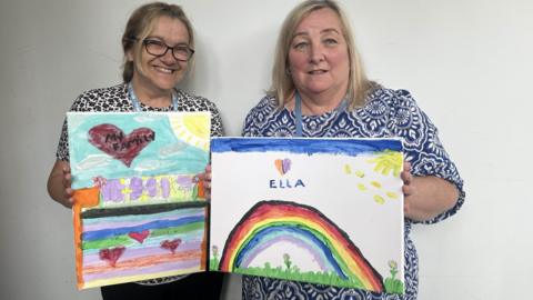 Jane and Tracy holding artwork made by children 