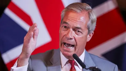 Nigel Farage gestures with his entire hand as he speaks at a podium at a press conference on August 10. He is dressed in a grey suit, white shirt and red tie with a union jack flag in the background