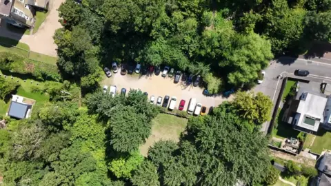 BBC A drone shot of mornington road car park with trees encircling the car park where cars can be seen.