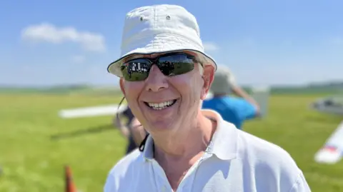 Club member, Mark Smallwood, smiling wearing black sunglasses, a white polo shirt and a white bucket hat