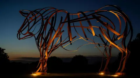 Cumberland Council An image of the bull statue, which is made out of metal strings assembled in the shape of a bull. In the picture, it is lit up at dusk.