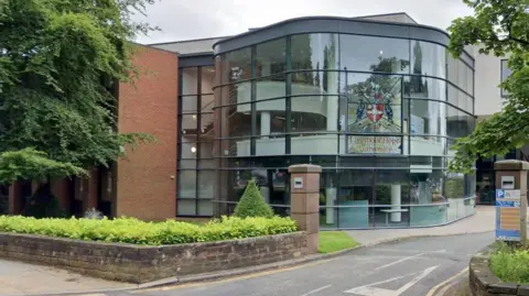 A glass fronted building set behind a sandstone wall entrance. A stained glass panel features the writing Liverpool Hope University along with the university crest.
