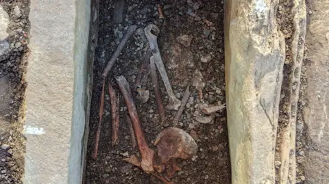 A burial cist, with bones visible - they are in the process of being excavated