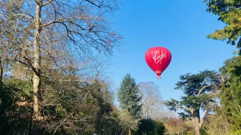 TAG A red Virgin branded balloon in the sky above a forest.