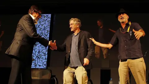 Hindustan Times via Getty Images A picture of Amitabh Bachchan, Robert De Niro and Tarun Tejpal on a black stage at a conference in India's Goa, 2013