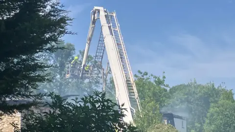 A ladder is suspending two firefighters in the air as they spray water over the scene. 