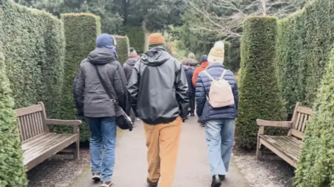 Three walkers in the middle of a park with their backs to the camera. 