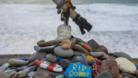 Getty Images A pile of colourful rocks with messages written on them including a blue one with RIP Dobby in yellow. the sea is in the background. 