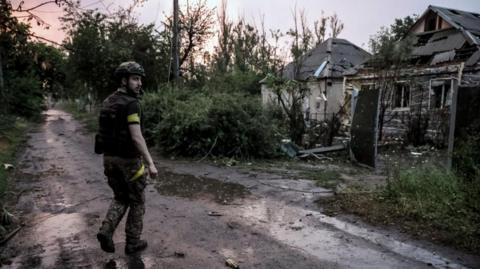 A Ukrainian serviceman stands in a road looking back, with houses to the side