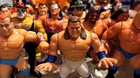 A collection figures of various wrestlers all standing in a huddle. They are bulky and muscly figures, rather cartoon like.