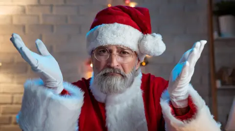 Getty Images Stock image of a man dressed as Santa Claus with his arms held up in a questioning pose