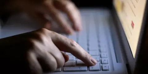 PA Media Two hands are seen on a keyboard with a laptop screen just visible