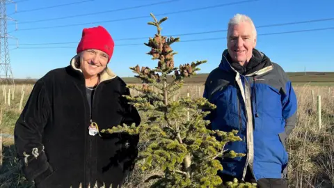 Nigel Stollery and Alison Stollery posing with their largest replanted Christmas tree.