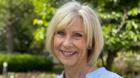 Aly Murphy is outside under the trees in the spring sunshine. She has bright blue eyes and blonde hair, and is smiling at the camera.