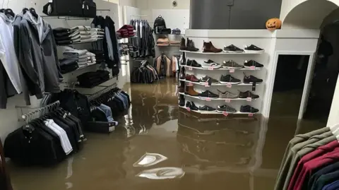 McCartan Bros Racks of clothes and shelves of shoes covered in floodwater