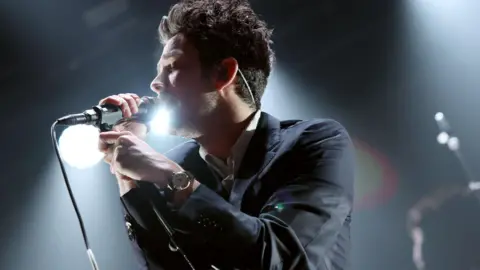 Matty Healy of The 1975 singing into a microphone on stage