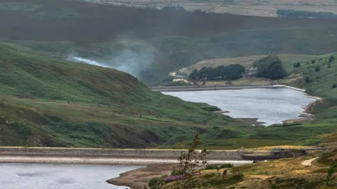 Rob Smith/BBC Smoke on a moorland with two reservoirs visible.