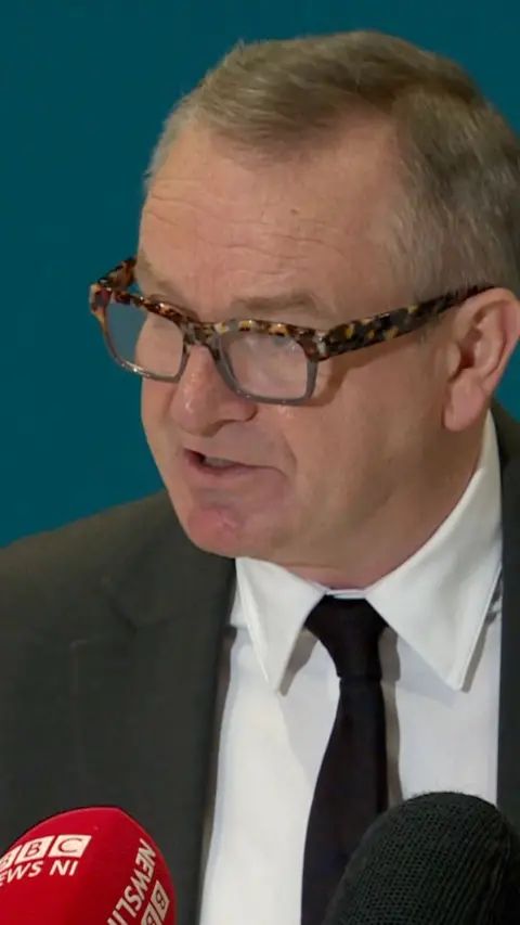 Sir Iain Livingstone wearing leopard print glasses and a shirt and tie
