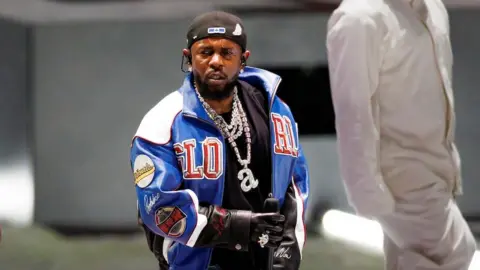 Getty Images Kendrick Lamar pictured wearing a blue leather jacket and lowercase a silver chain.